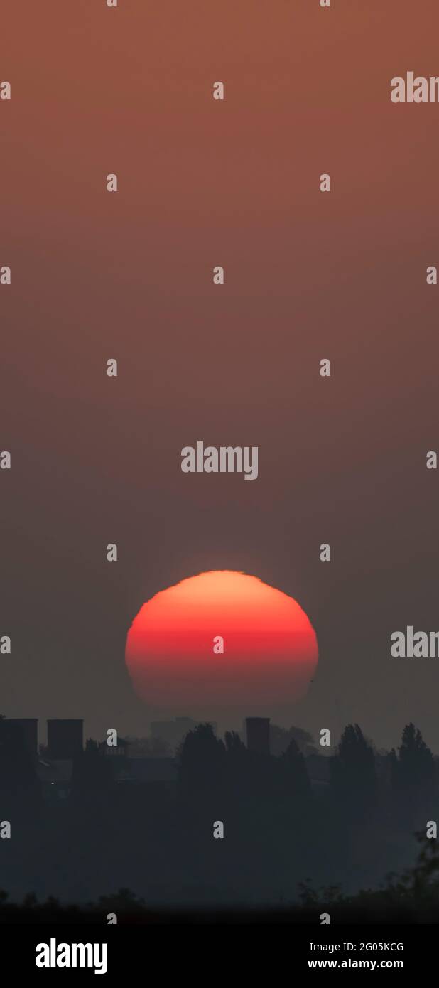 Wimbledon, London, UK. 1 June 2021. The rising sun contorts in shapes as it moves through thick layers of atmosphere over rooftops near the horizon above London before it begins a day of mini heatwave temperatures. Credit: Malcolm Park/Alamy Stock Photo