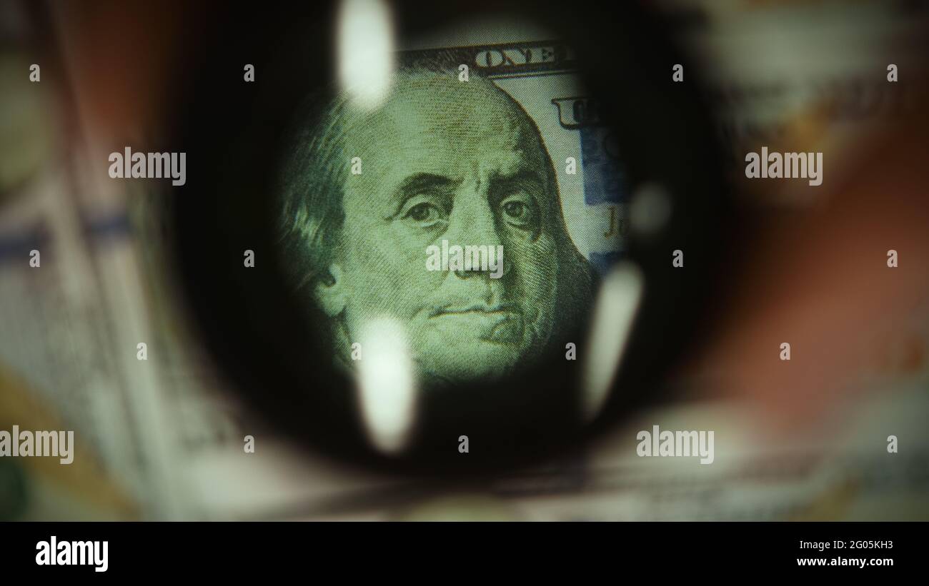 Front side of hundred dollar banknotes examine with magnifying glass, concept of counterfeit money and finance Stock Photo