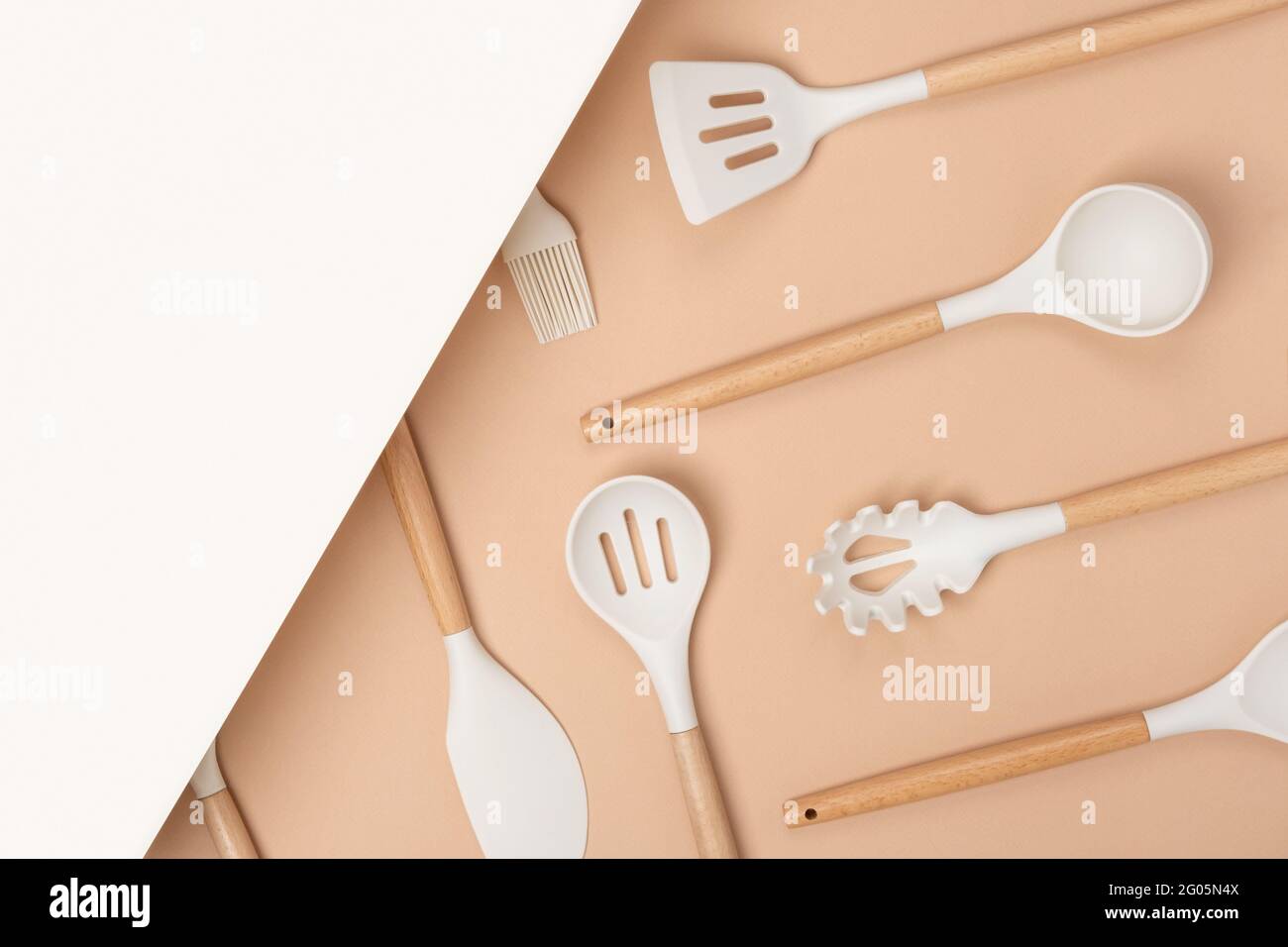 Cooking utensil set. Silicone kitchen tools with wooden handle on beige background with copy space. Top view Flat lay. Stock Photo