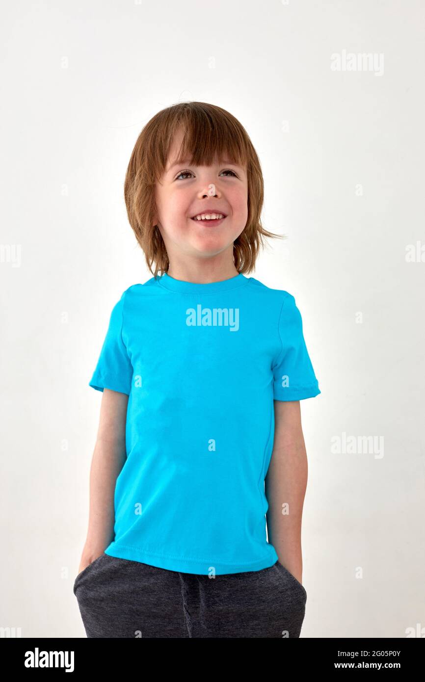 Glad young boy in blue t shirt standing against white background and looking away Stock Photo