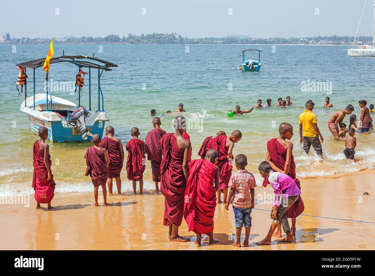 Group of young novice Buddhist monks wearing maroon robes paddling barefoot in the sea, Jungle Beach, Unawatuna, Southern province, Sri lanka Stock Photo