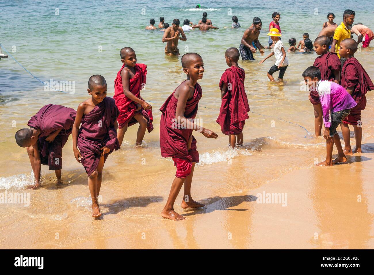Group of young novice Buddhist monks wearing maroon robes paddling barefoot in the sea, Jungle Beach, Unawatuna, Southern province, Sri lanka Stock Photo