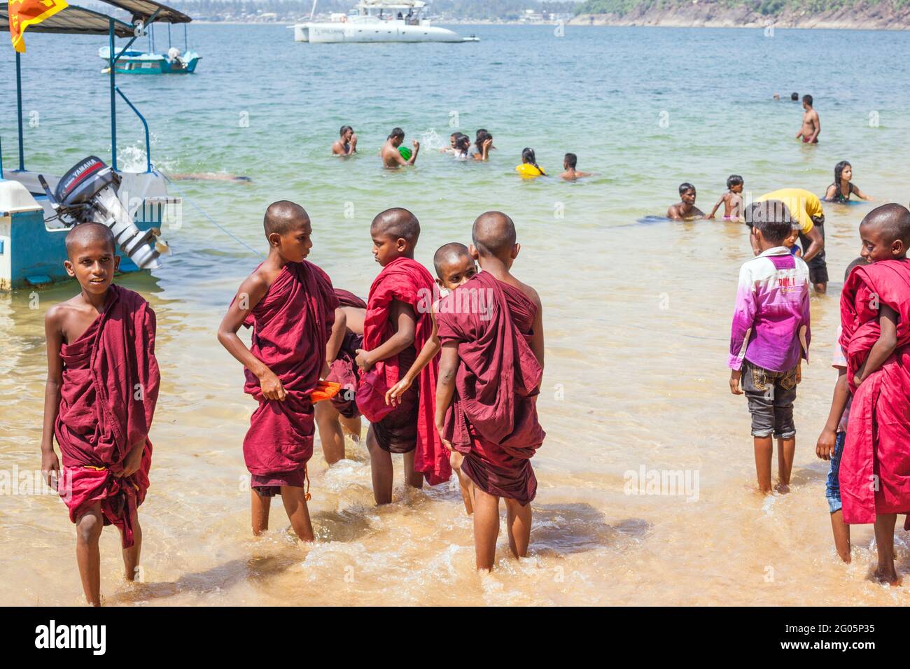 Group of young novice Buddhist monks wearing maroon robes paddling barefoot in the sea, Jungle Beach, Unawatuna, Southern province, Sri lanka Stock Photo