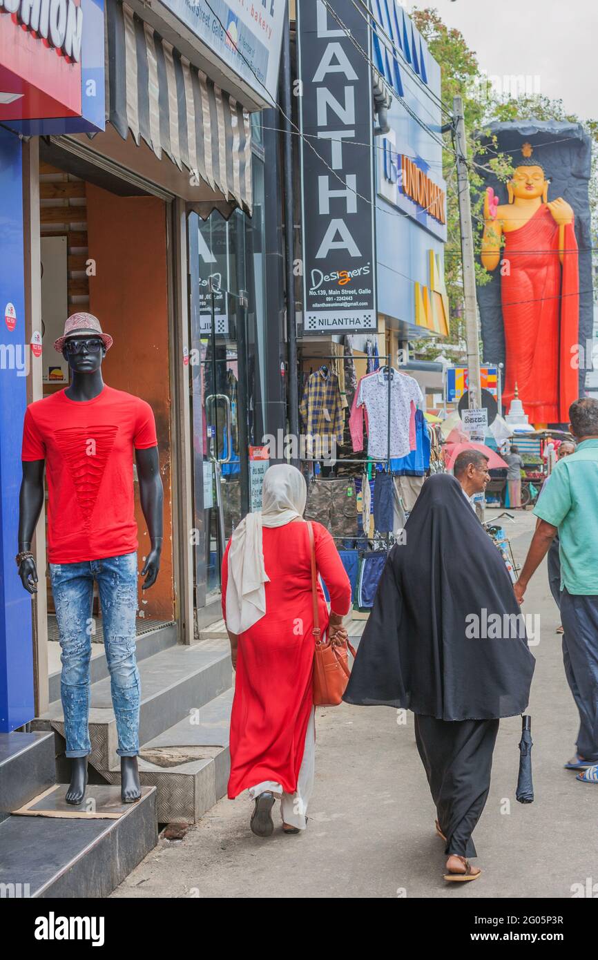 Black mannequin outside shop with Muslim female in black burqa walking towards Galu Maha Bodiya Buddhist statue, Galle, Southern province, Sri Lanka Stock Photo