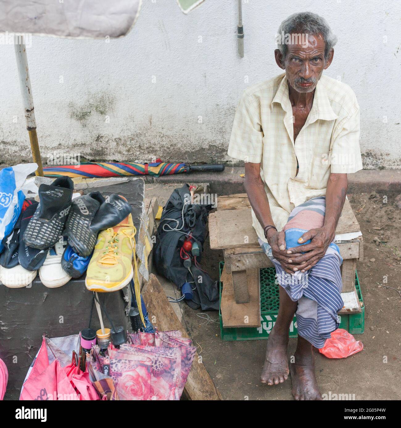 Unhappy Sri Lankan male shoe salesman vendor with dented skull sits beside his stock, Unawatuna, Southern Province, Sri Lanka Stock Photo