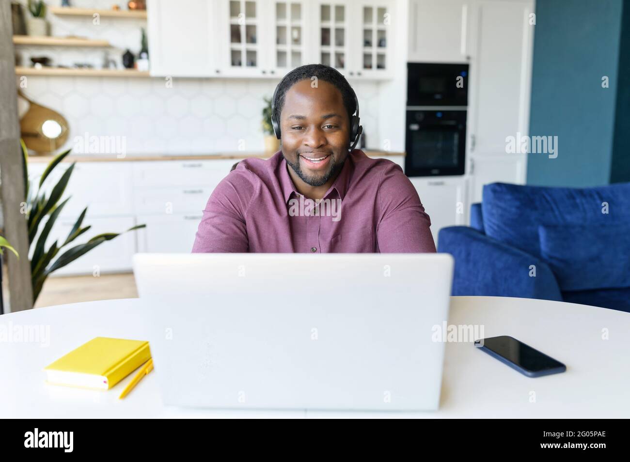 Guy in wirelessheadset using laptop sitting in the kitchen home. Remote work concept Stock Photo