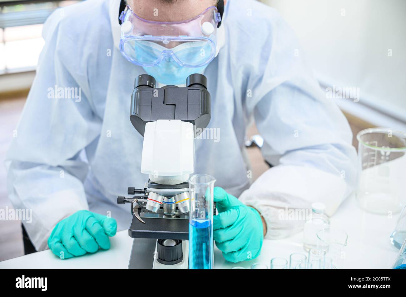 Male scientist wearing protection suit working with microscope and many
