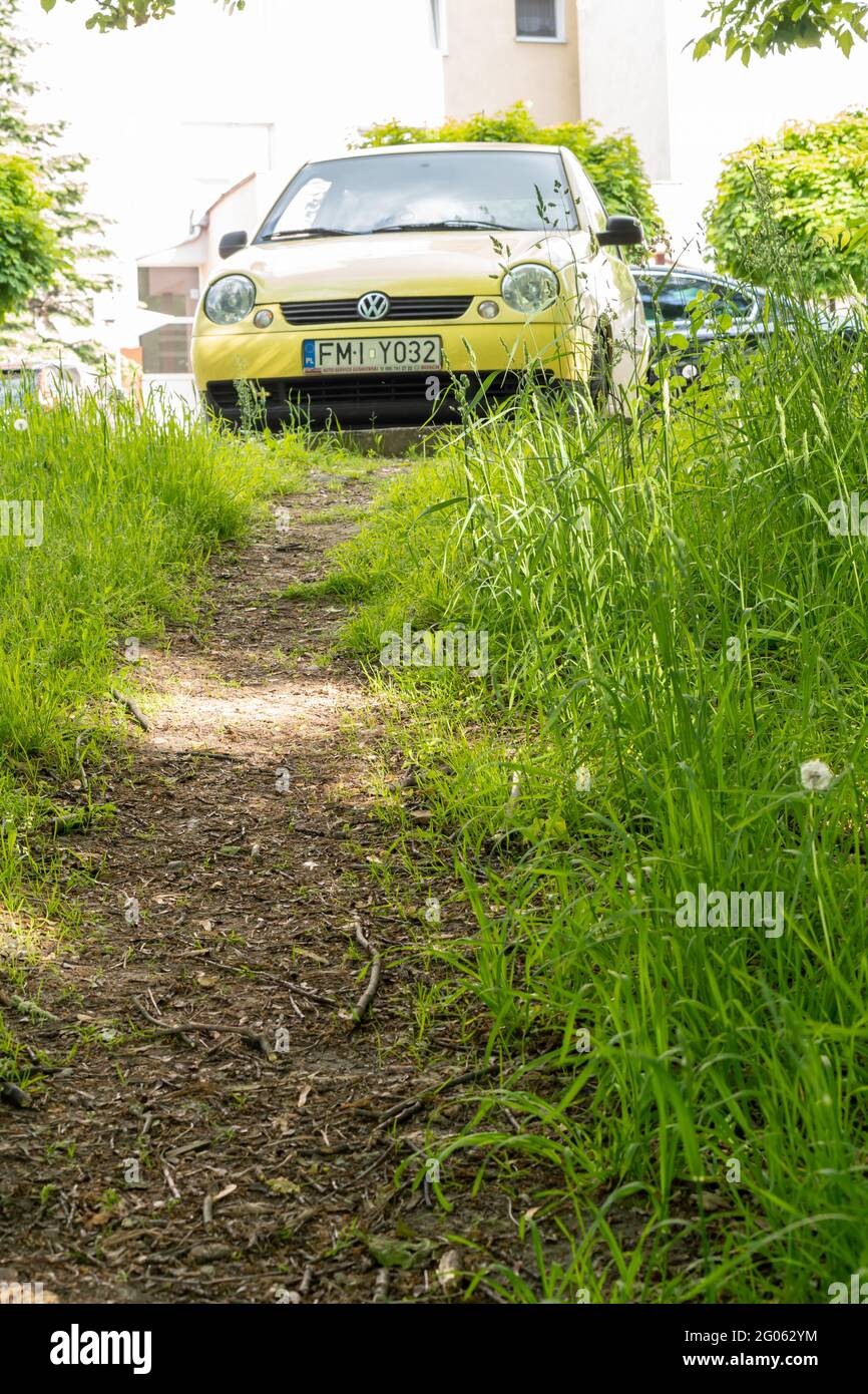 POZNAN, POLAND - May 31, 2021: Small path along green grass leading to a yellow parked Volkswagen Lupo car in the city. Stock Photo