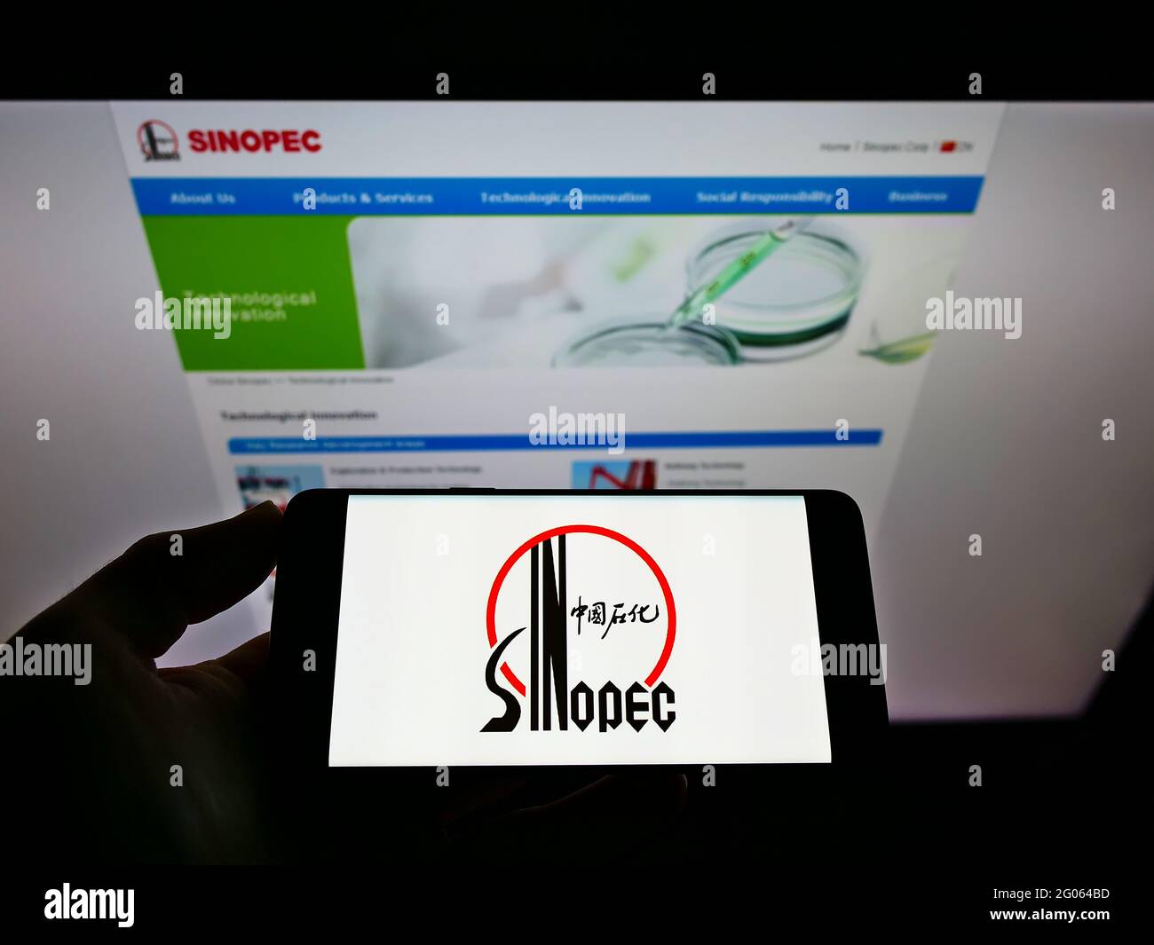 Person holding mobile phone with logo of company China Petrochemical Corporation (Sinopec) on screen in front of web page. Focus on phone display. Stock Photo