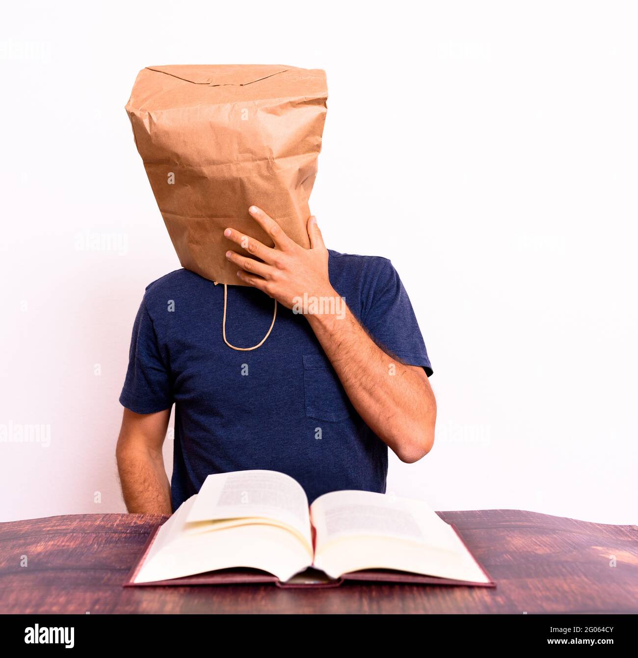 Funny man with his head covered with a paper bag reading and studying a book. Stock Photo