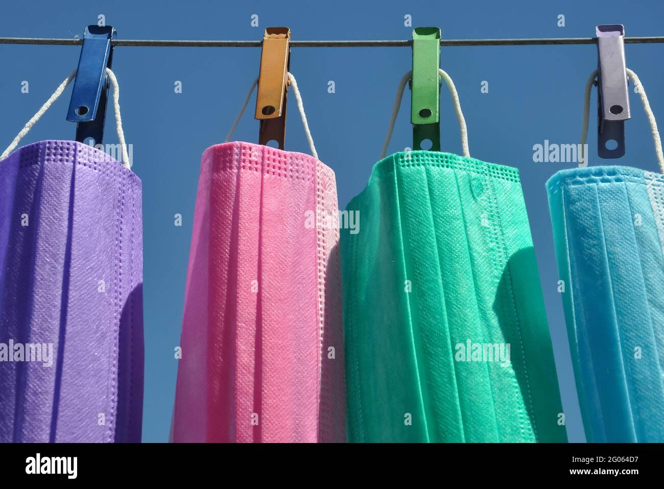 Front view of multi colored surgical face mask (Disposable mask) hanging on clothesline wire with clothespin, Concept of protect environment from waste and pollution. Stock Photo