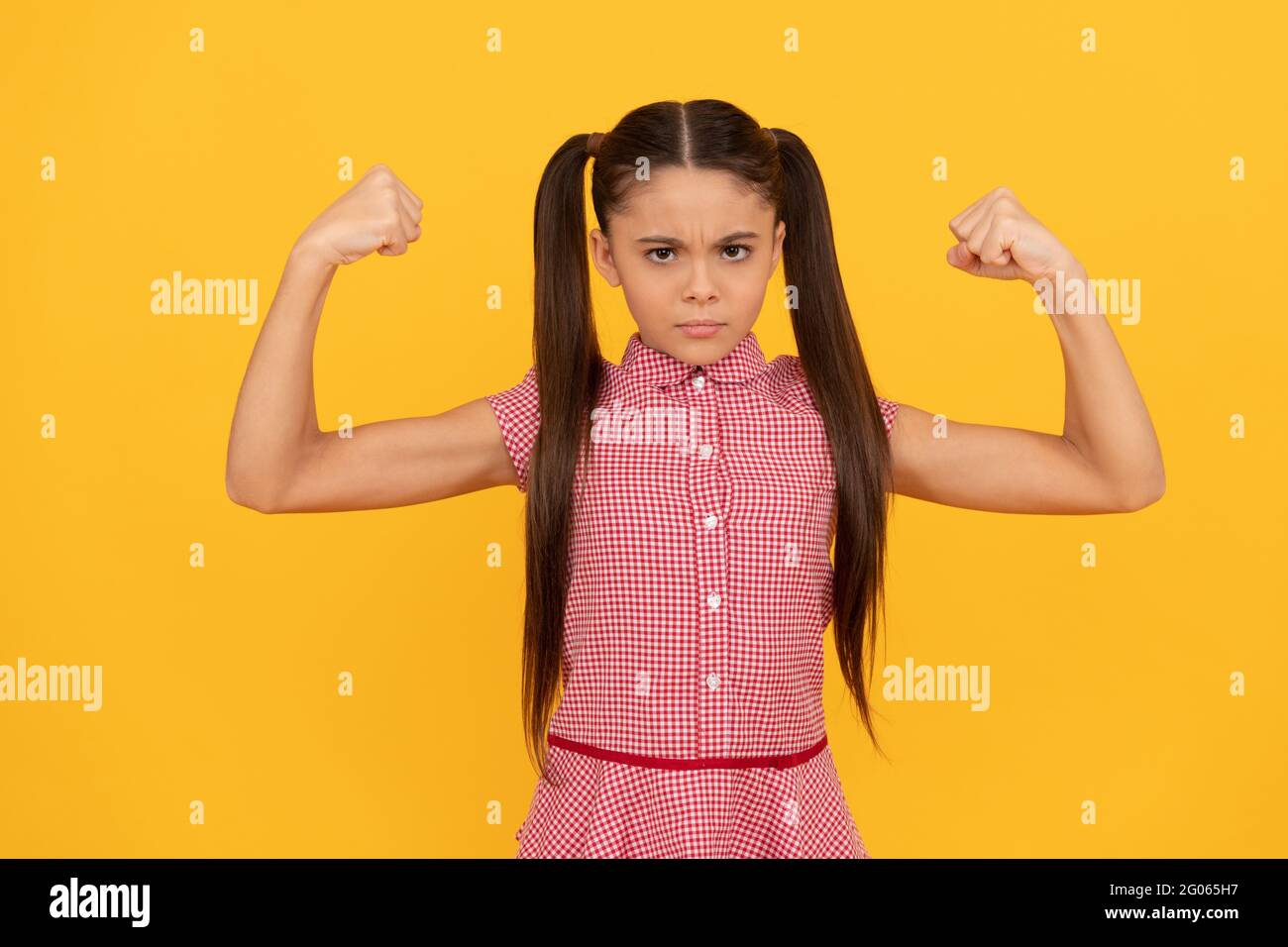 Serious girl child show strength gesture flexing arms yellow background, girl power Stock Photo