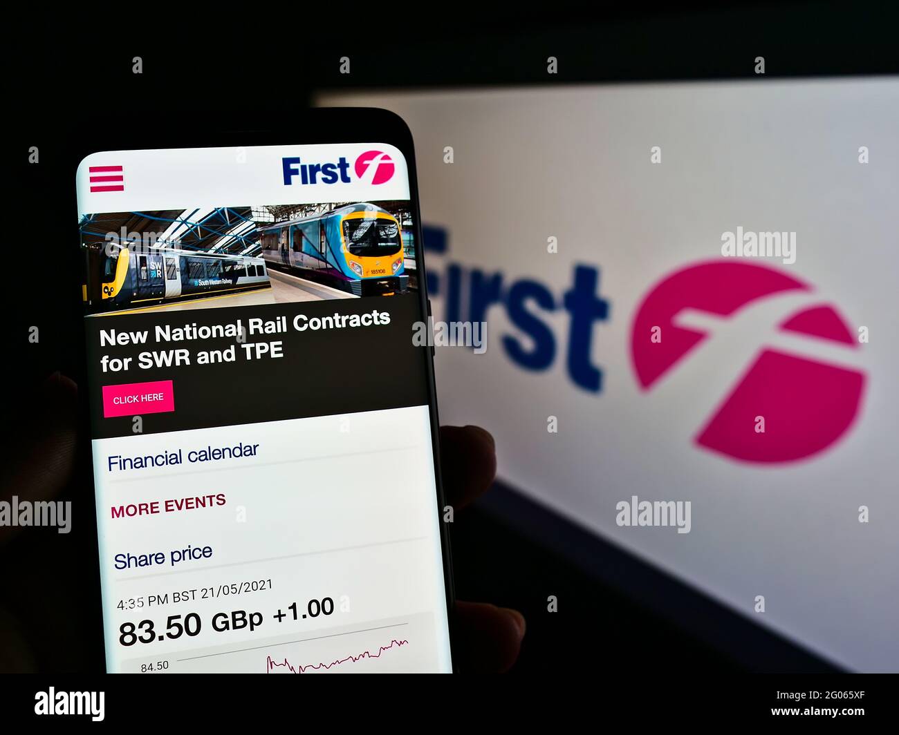 Person holding cellphone with web page of British transport company FirstGroup plc on screen in front of logo. Focus on center of phone display. Stock Photo