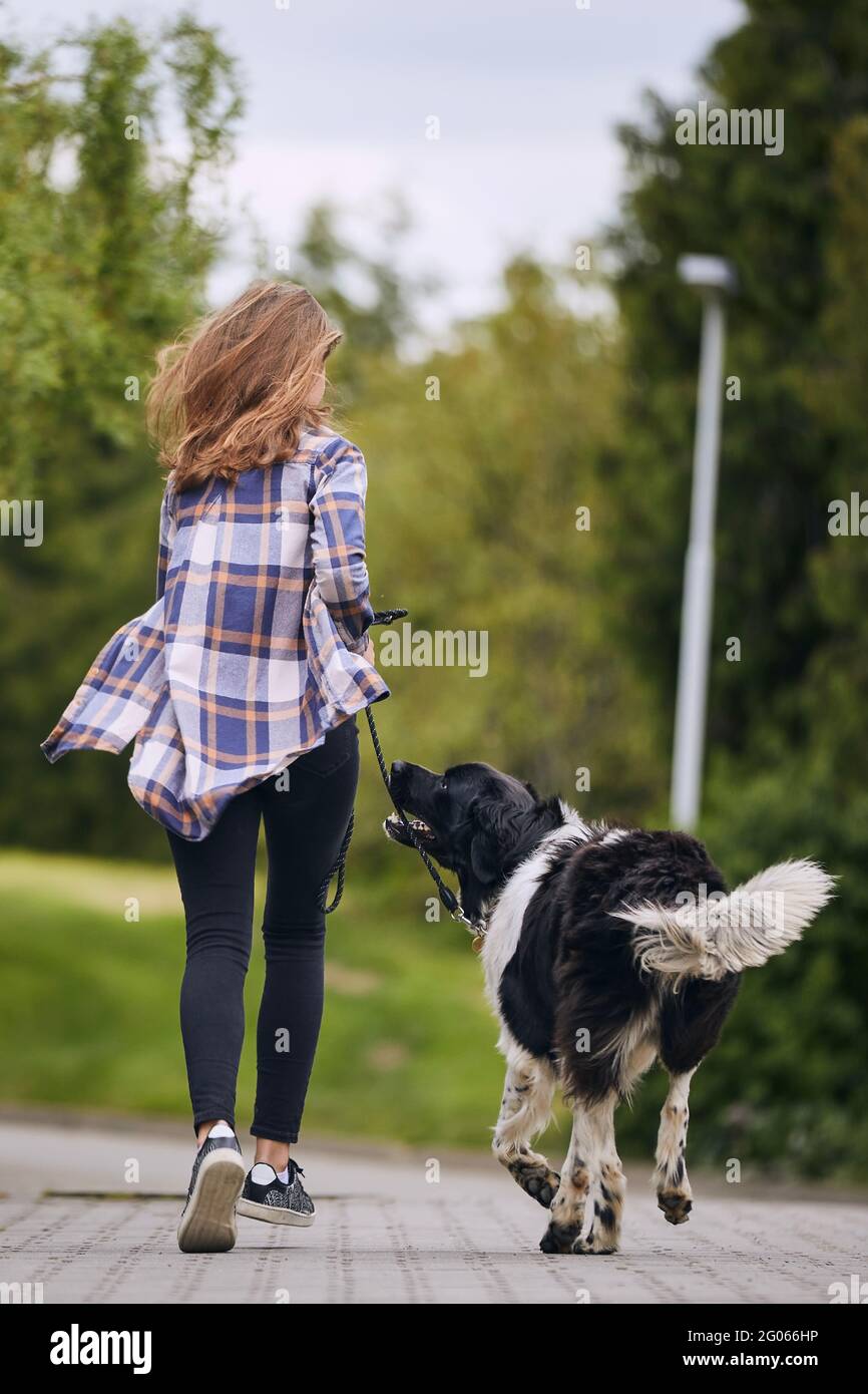 Rear view of teenage girl running with her dog on pet leash down street