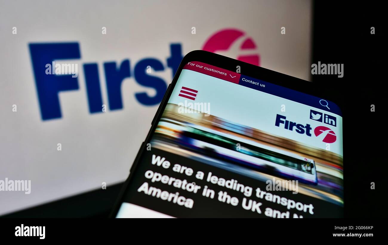 Mobile phone with website of British transport company FirstGroup plc on screen in front of business logo. Focus on top-left of phone display. Stock Photo