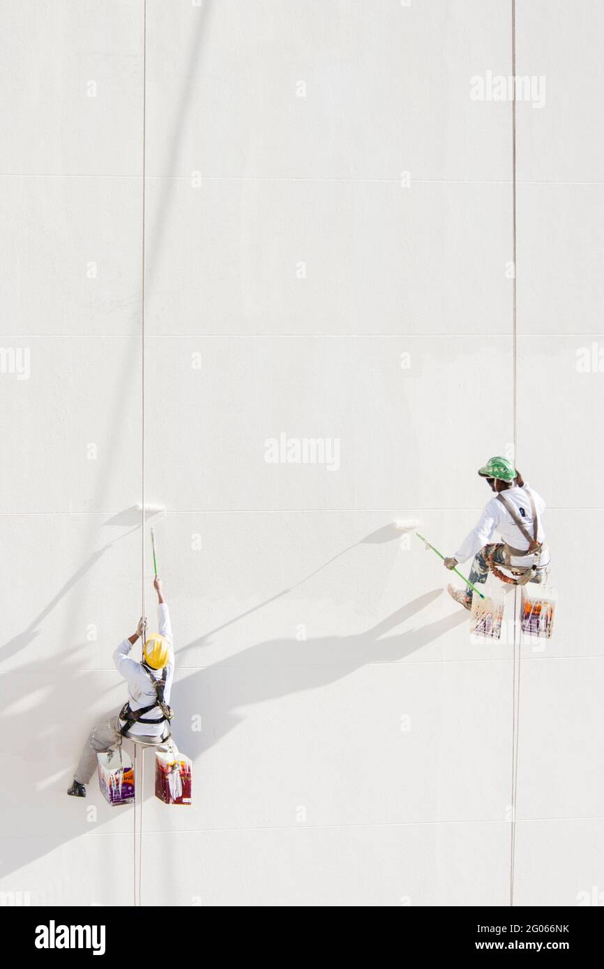 workers painting a tall building, hanging from ropes Stock Photo