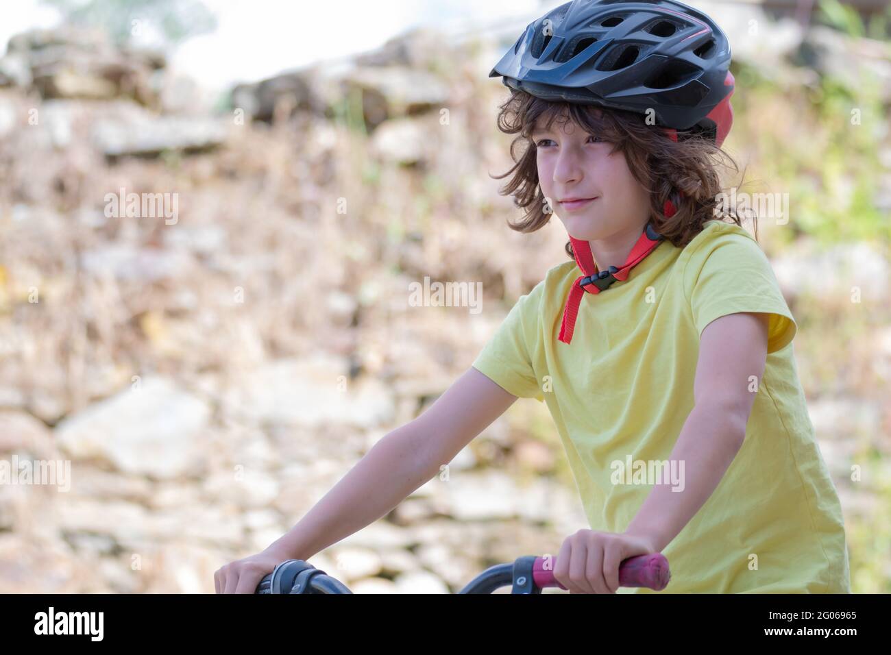 smiling boy in red helmet and yellow t-shirt has fun riding bike on sunny day Stock Photo