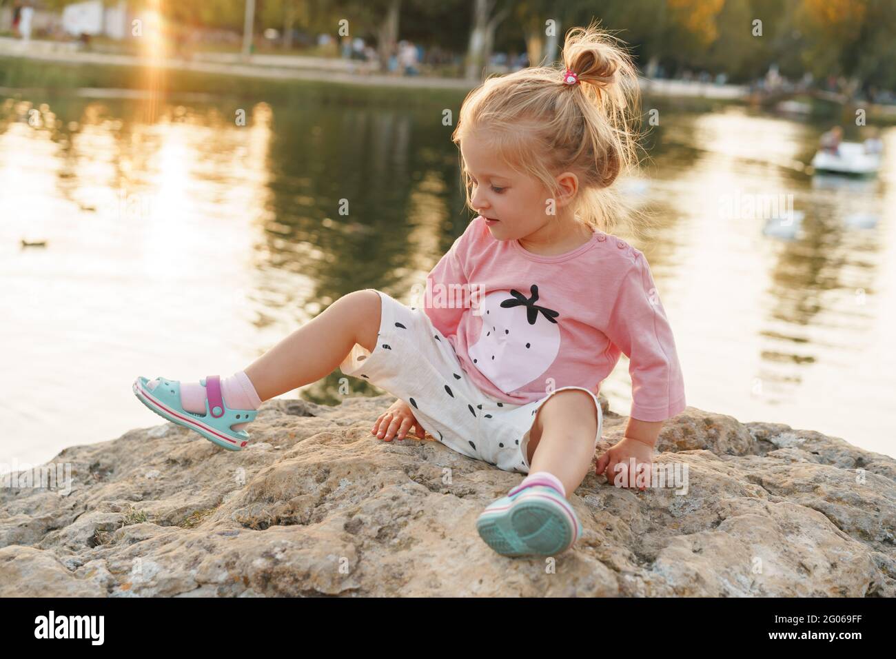 Little girl sitting on a huge stone in park near the lake Stock Photo ...