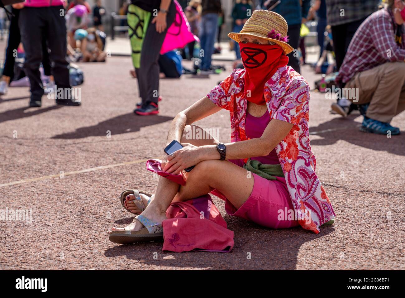 LONDON, UK - Extinction Rebellion activist sits on the pavement wearing colorful clothes and a face covering during a climate change protest Stock Photo