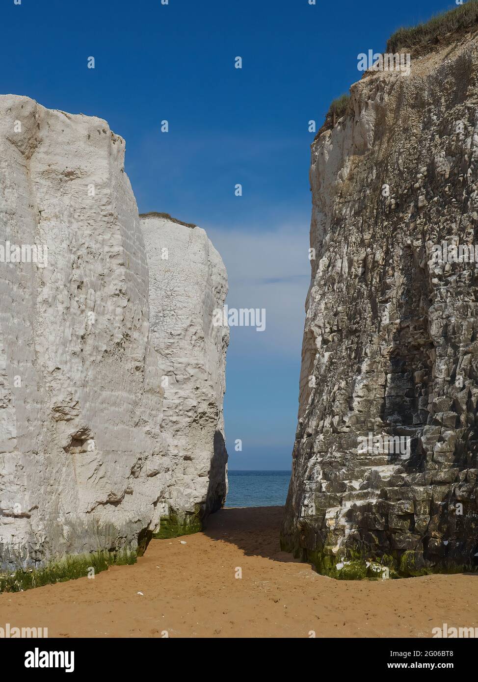 A snatch of blue sea between two white chalk cliffs with golden sands underneath and a summery blue sky overhead. Stock Photo
