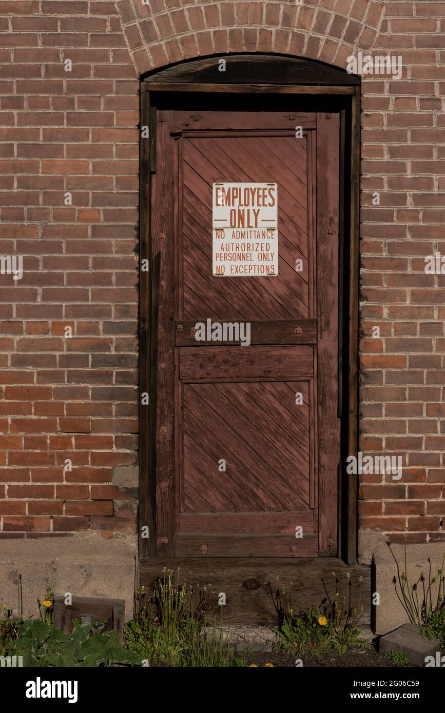 A sign on a old wooden door of a brick building reads employees only. Stock Photo