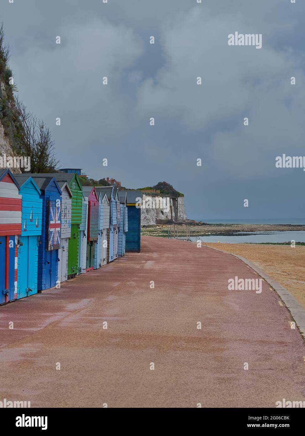 Stone Bay’s sweeping curved path, with its cliffs, sands and brightly coloured beach huts, under a heavy, clouded sky. Stock Photo