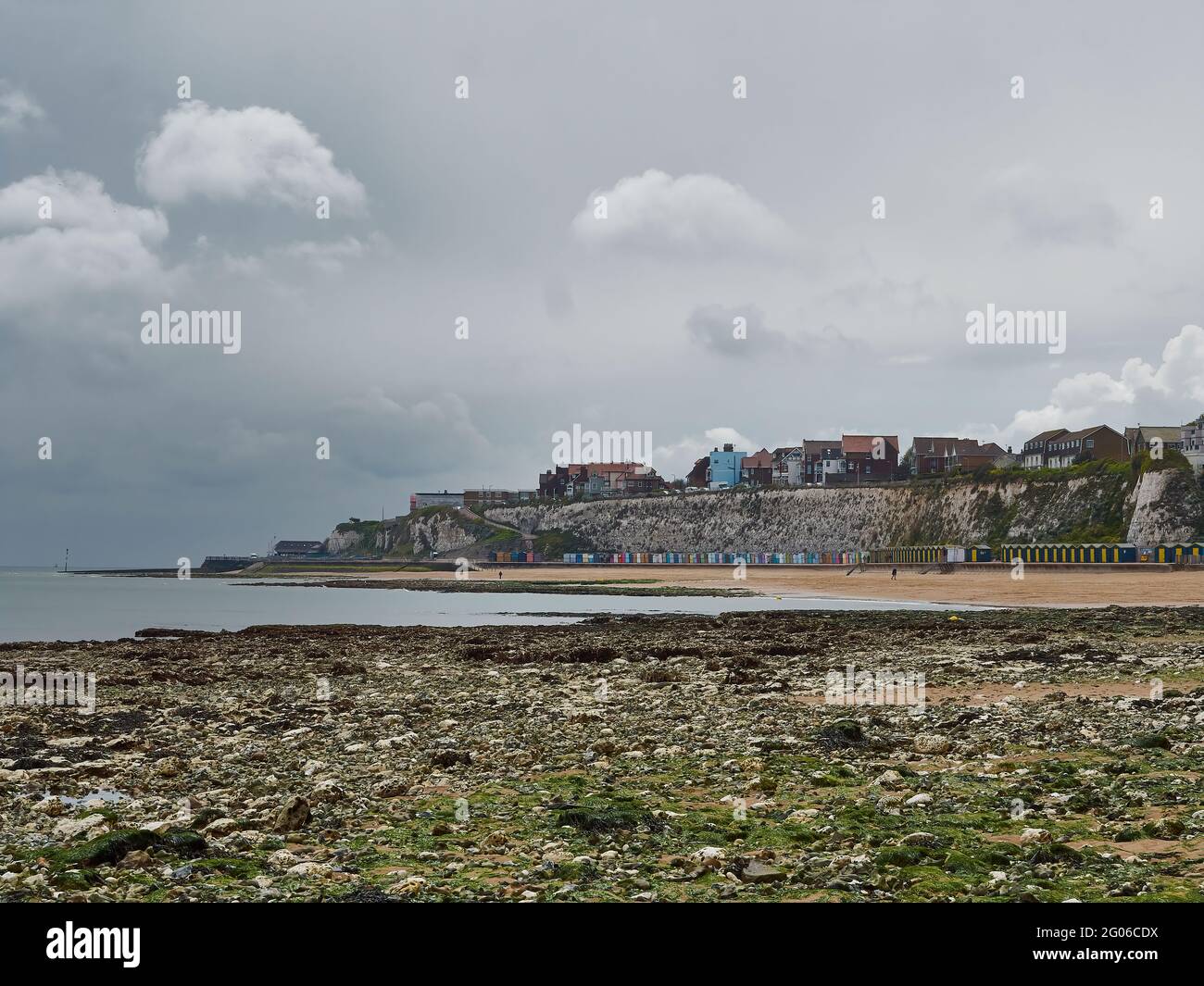 A muted view across Stone Bay’s beach, chalk cliffs and colourful beach huts, to the far headland, all under a heavy, oppressively clouded sky. Stock Photo
