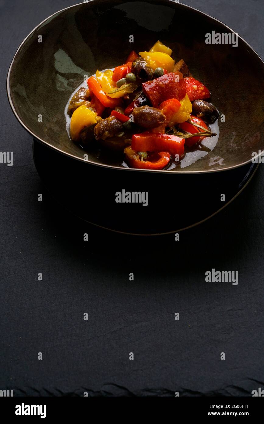 Traditional sicilian Caponata with red and yellow peppers, cherry tomatoes, black olives, capers, rosemary Stock Photo