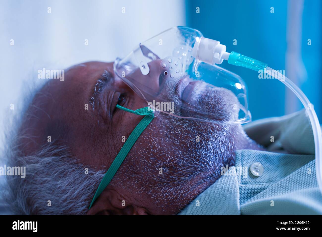 Close up head shot side view of old man breathing with ventilator oxygen mask at hospital due to coronavirus covid-19 lung infection, breath shortness Stock Photo
