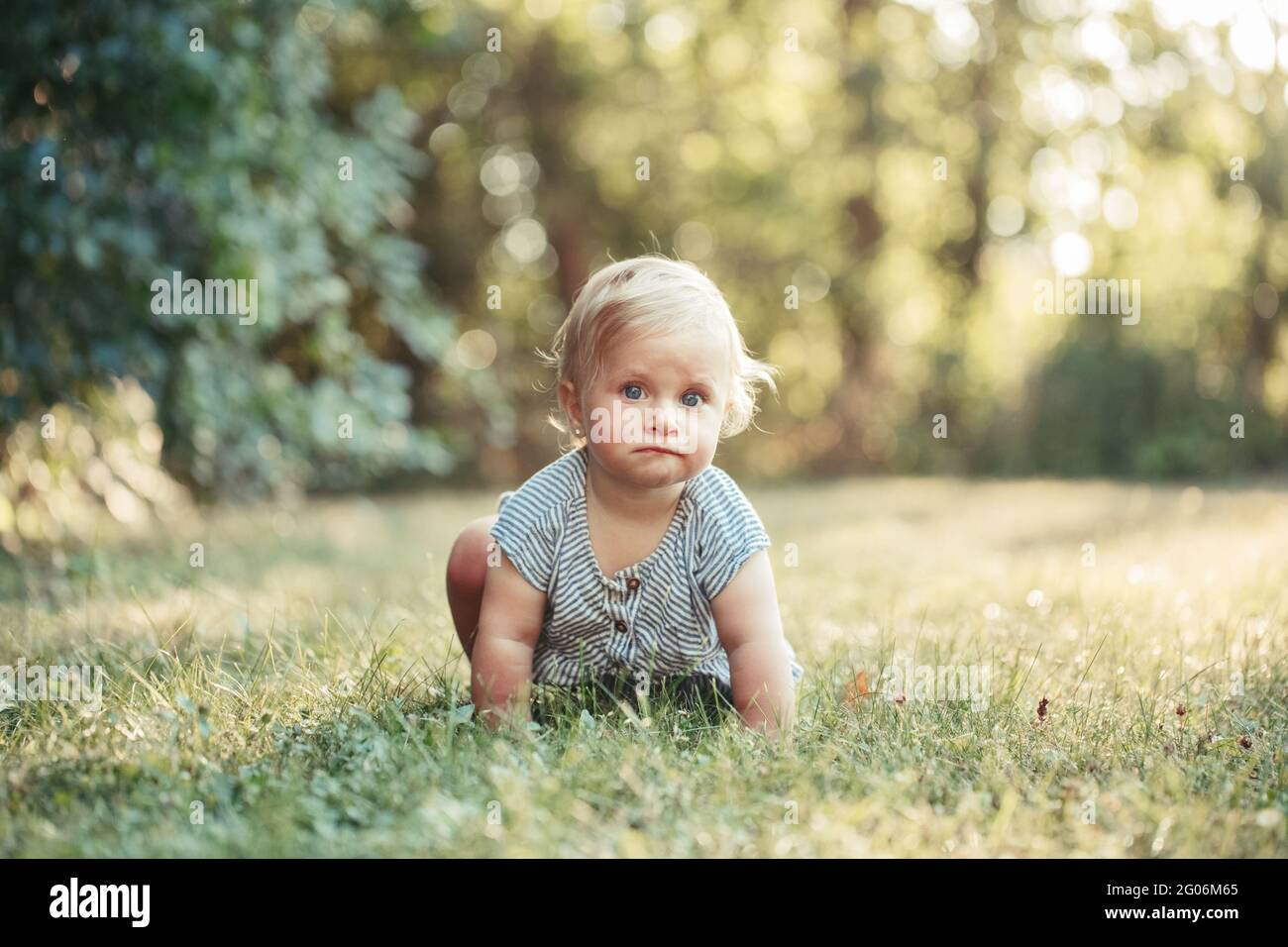 Cute baby girl crawling on ground in park outdoors. Adorable child toddler learning to walk outside. Healthy physical development. Funny surprised Stock Photo