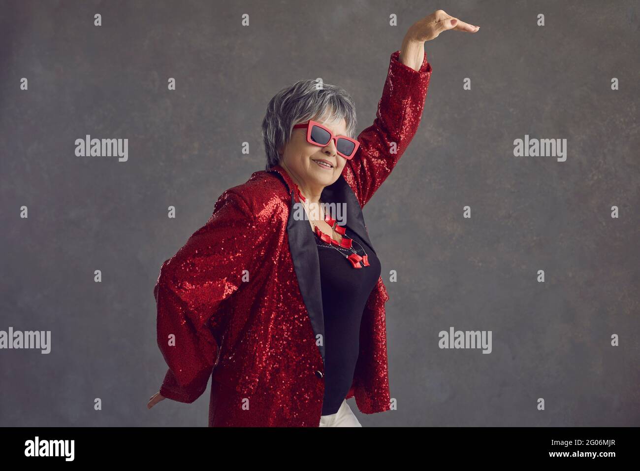 Side view of happy senior woman in red sequin jacket dancing on gray studio background Stock Photo