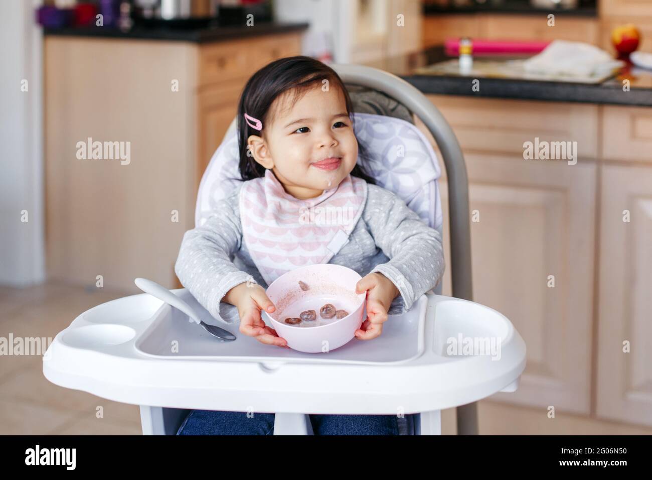 Cute adorable Asian Chinese kid girl sitting in high chair eating soup with spoon. Healthy eating for kids children. Toddler eating independently in k Stock Photo