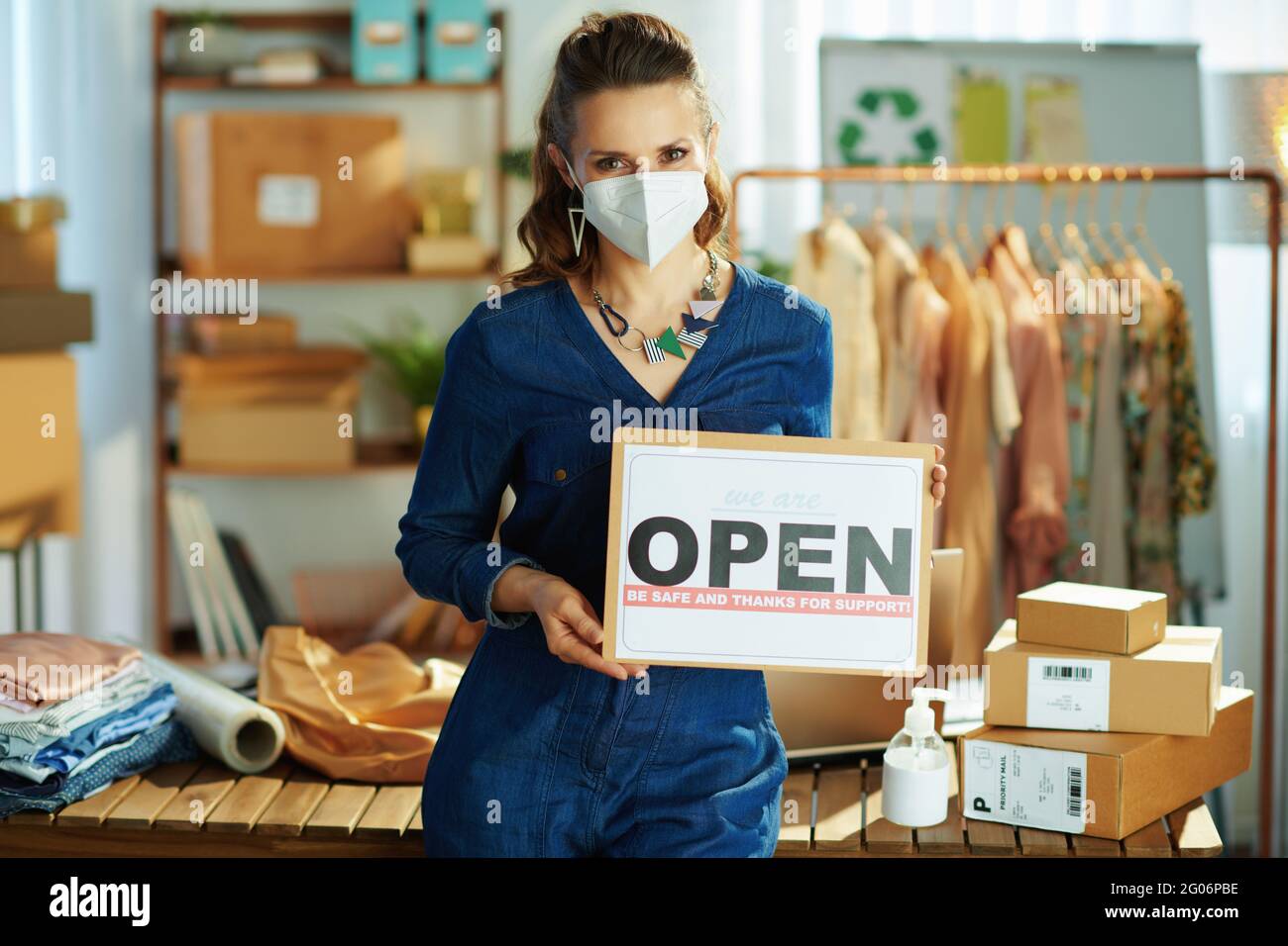 trendy small business owner woman with ffp2 mask, open after covid sign and antiseptic in the office. Stock Photo