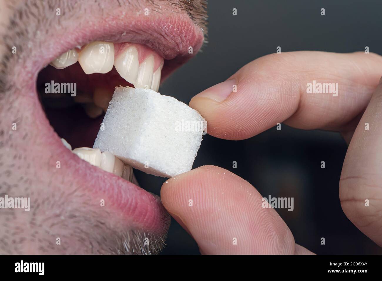 man's mouth with white teeth bites on a white sugar cube. Close up ...
