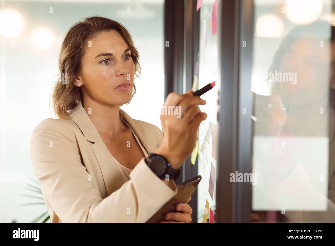 Caucasian businesswoman making notes and adding post-ins on transparent board Stock Photo