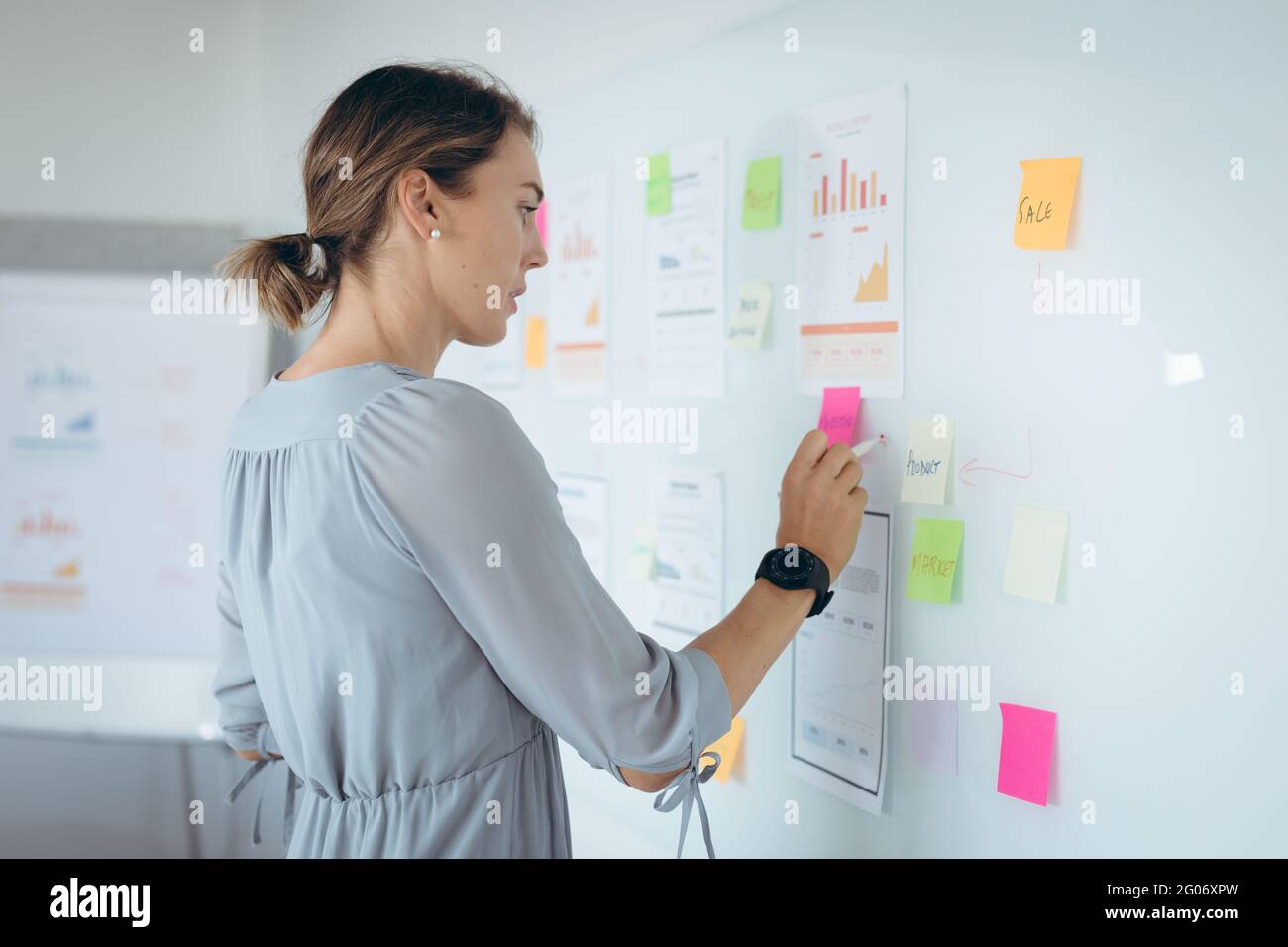 Caucasian businesswoman making notes and add post-ins on wall Stock Photo