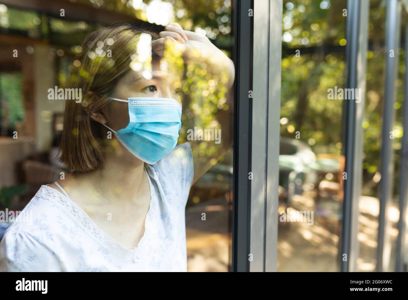 Sad asian woman wearing face mask and looking out of window Stock Photo