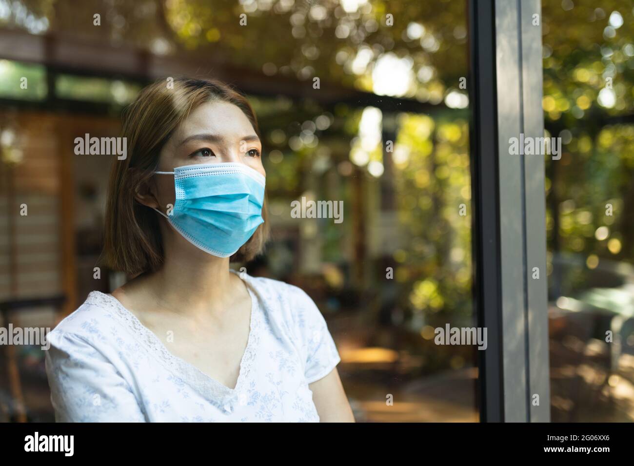 Sad asian woman wearing face mask and looking out of window Stock Photo