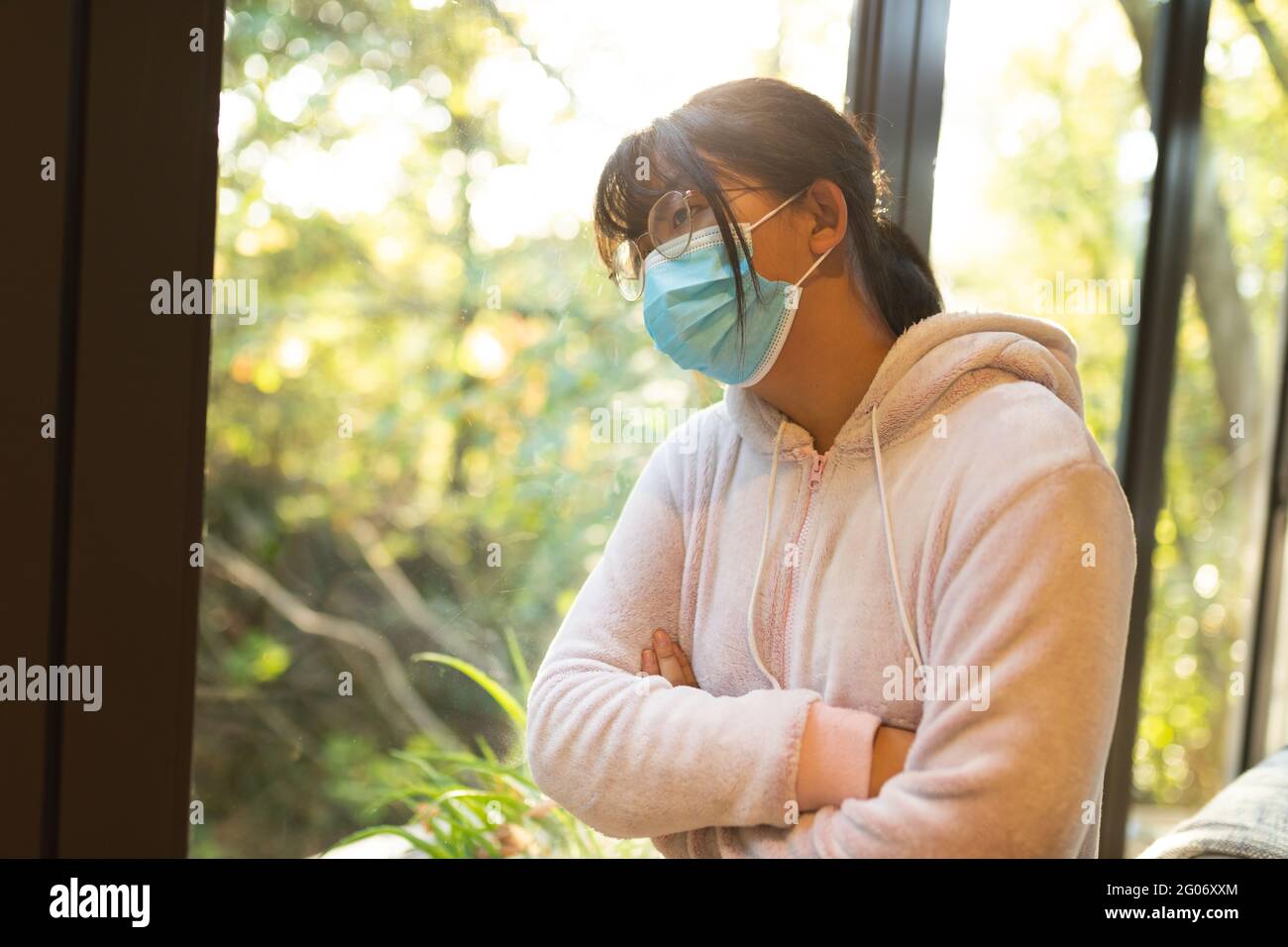 Sad asian girl in glasses wearing face mask and looking out of window Stock Photo