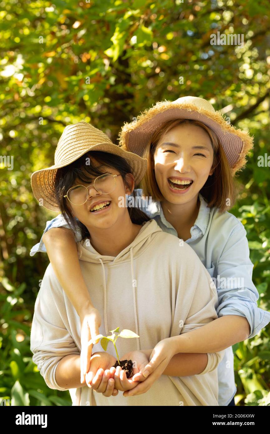 Smiling asian woman with hers daughter wearing straw hats and holding plant in garden Stock Photo