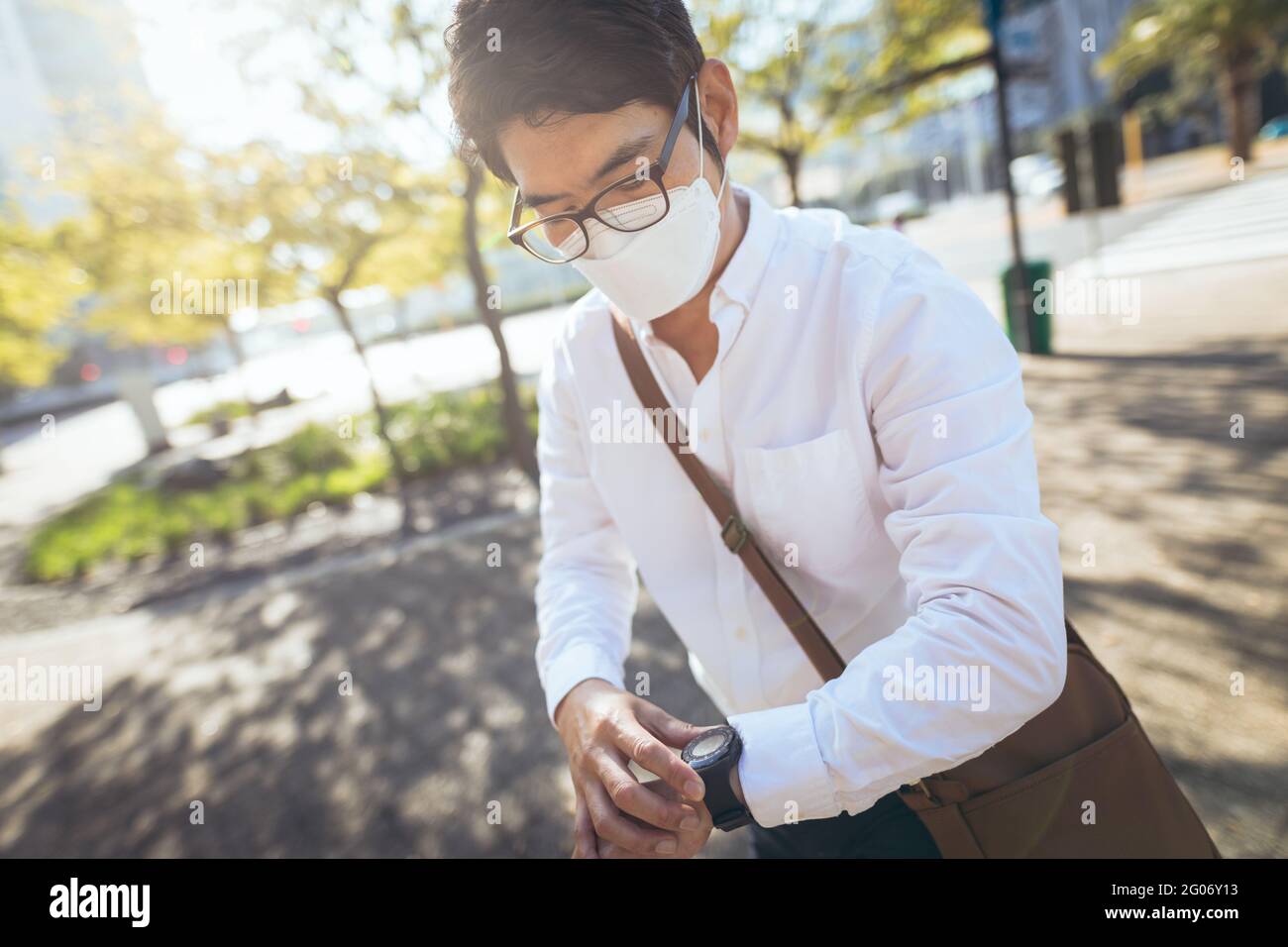 Asian businessman wearing face mask using smartwatch in city street ...