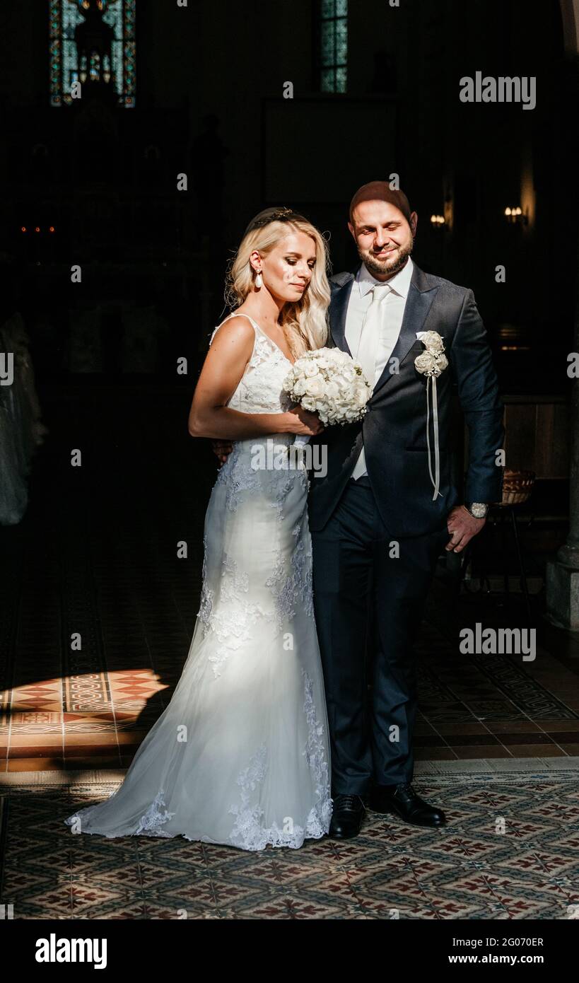 Full length portrait of bride and groom standing on church entrance with natural light. Stock Photo
