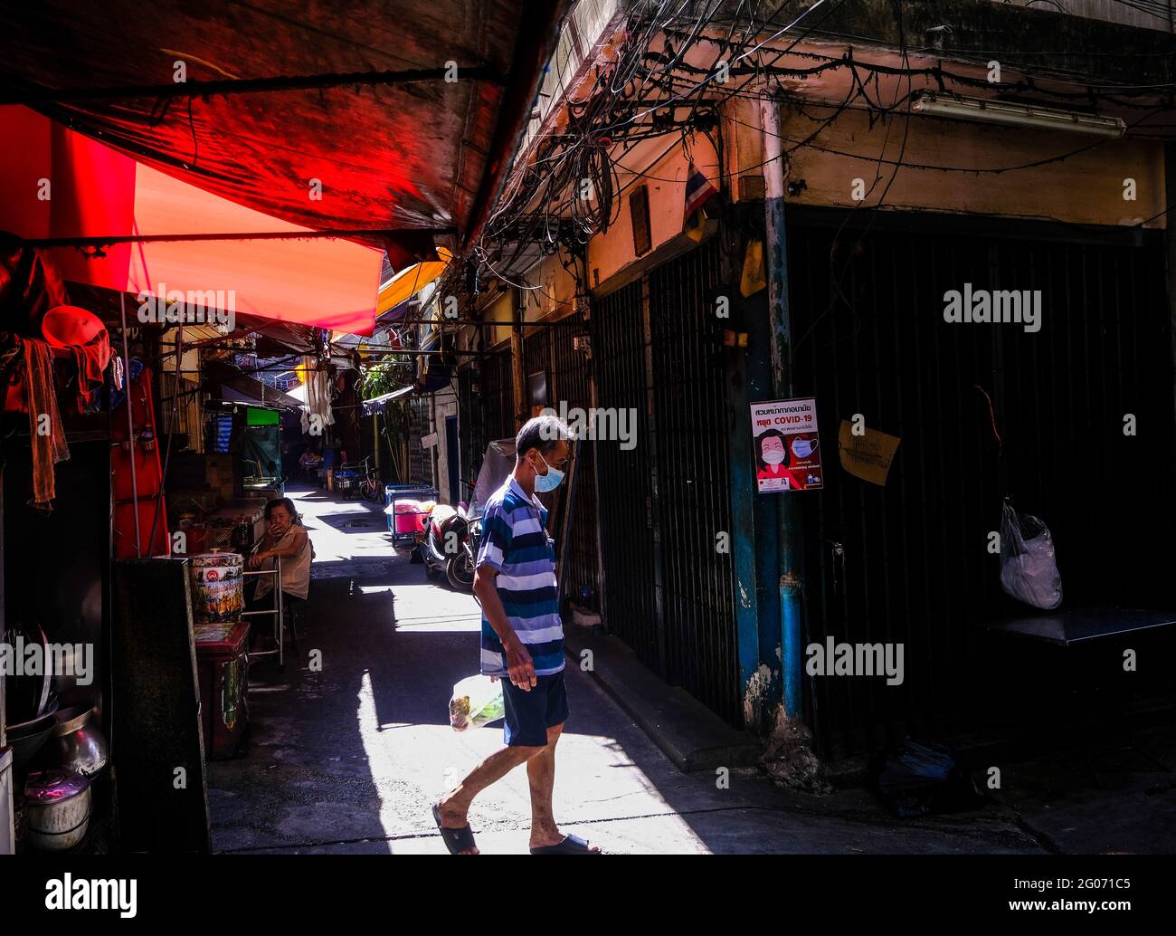 A man walks across a sunlit alley in Chinatown, Bangkok, Thailand Stock Photo