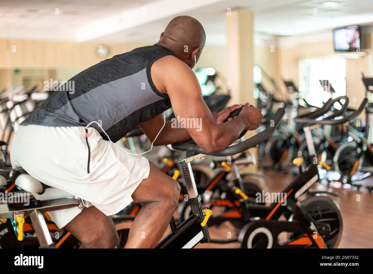 View of unrecognizable black person doing exercise bike in fitness center. Healthy lifestyle concept. Stock Photo