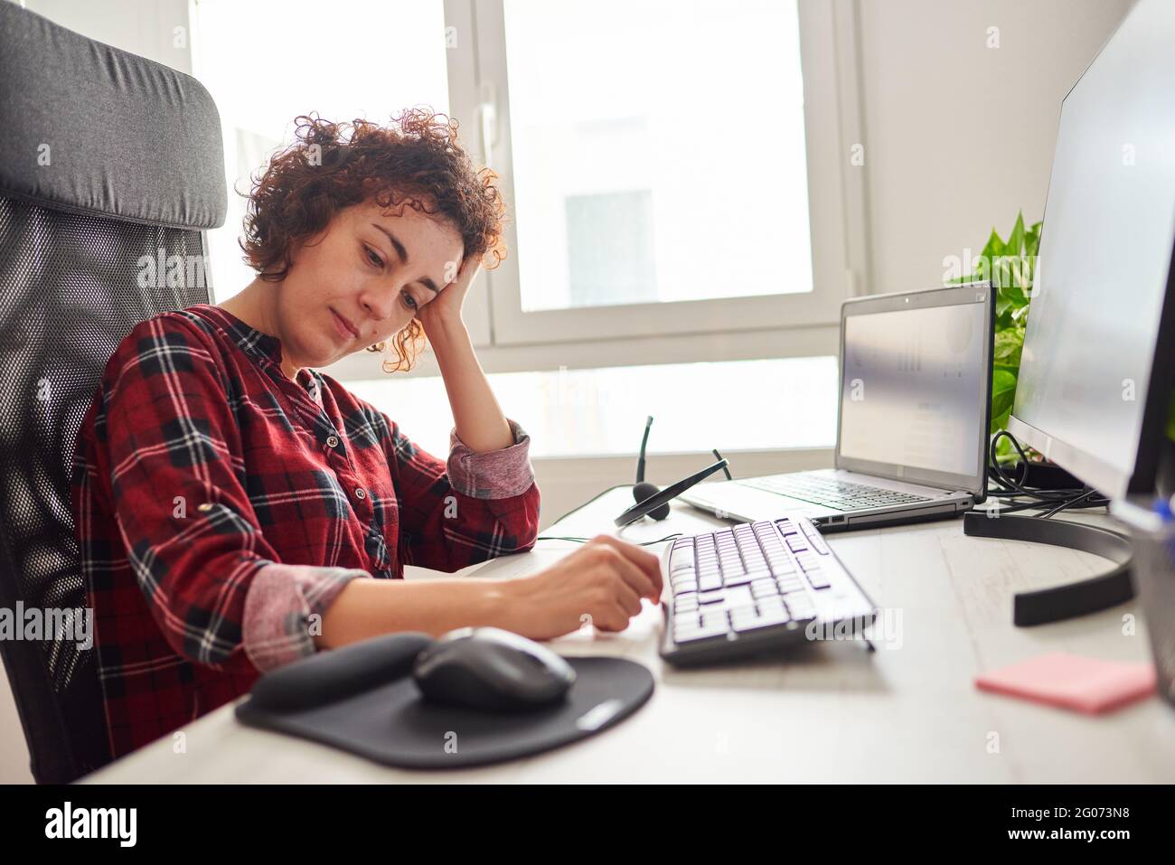 Woman tired of working in front of the computer rests her head on her hand Stock Photo