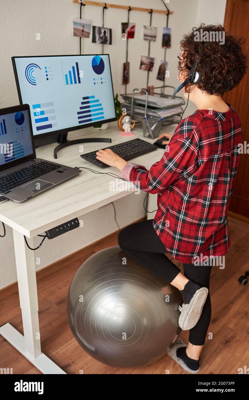 Woman working standing from home with an adjustable height desk and resting her knee on a fitball Stock Photo