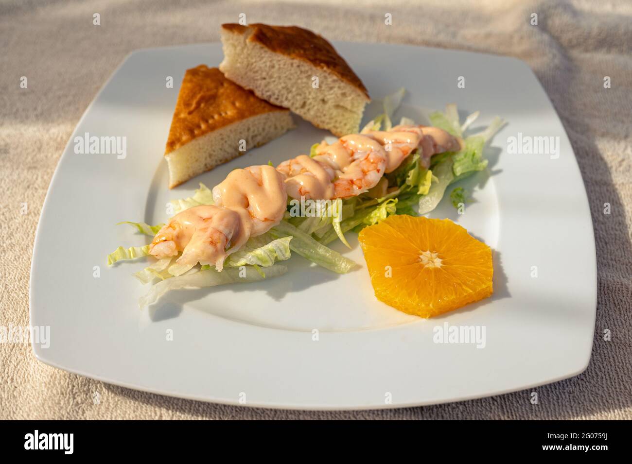 Boiled prawn shrimps on white plate. Shrimps with sauce on a white plate are laid out on lettuce leaves, decorated with orange. snacks on the beach. l Stock Photo