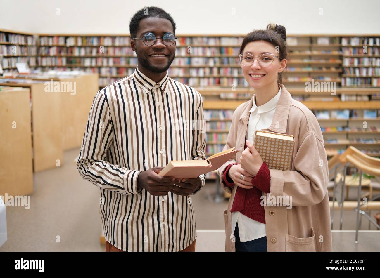 two smiling students holding books at campus Stock Photo - Alamy