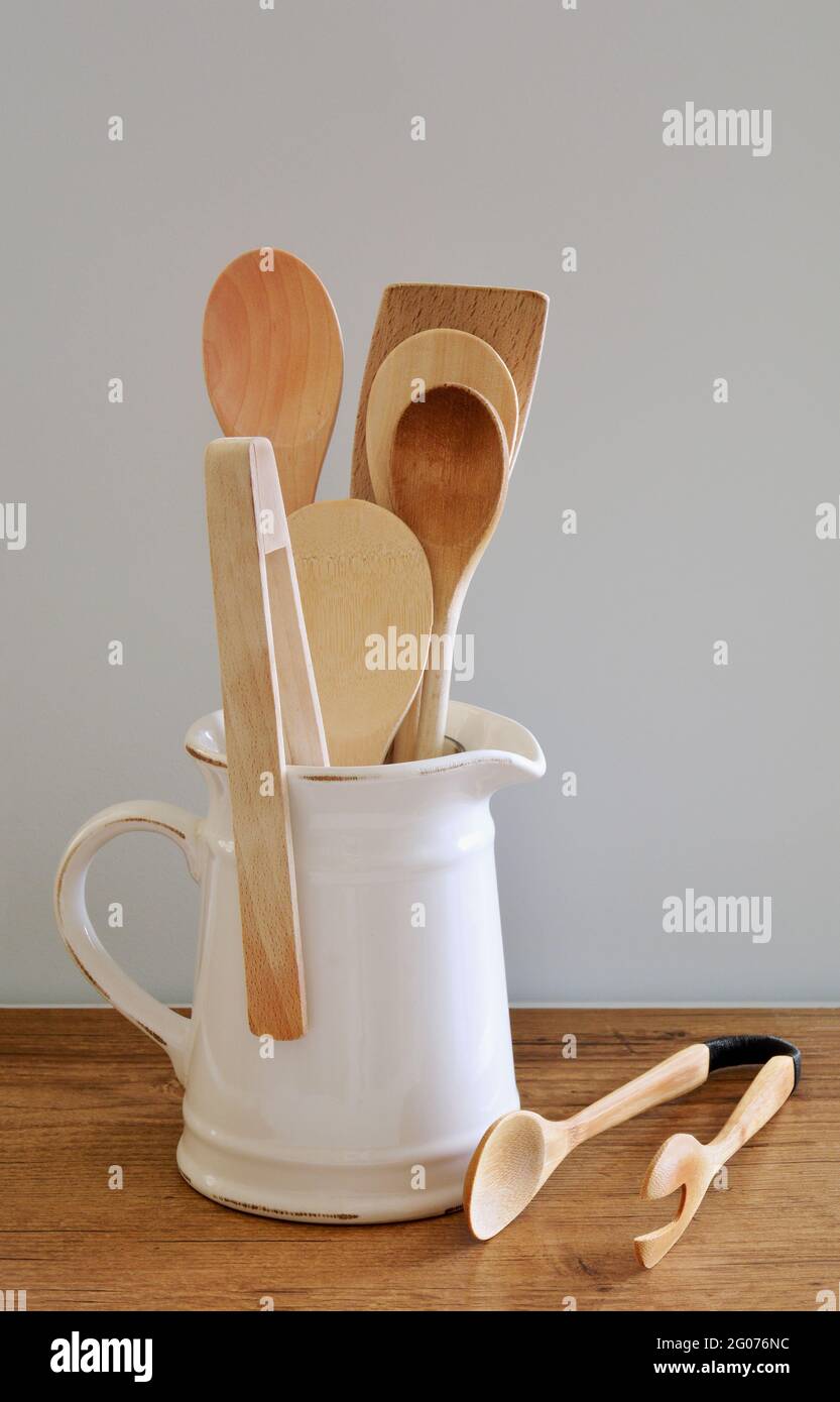 Wooden kitchen utensils in white rustic jug in vertical format. Natural light. Kitchen decor. Room for text. Stock Photo