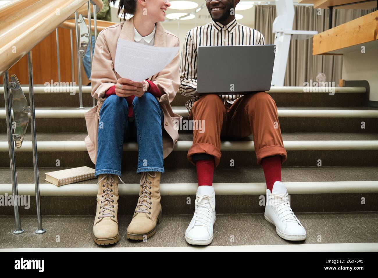 Young couple with laptop and documents sitting on stairs and studying in team Stock Photo